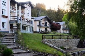 Um hotel com vários andares, varandas, um muro de pedra e uma escadaria que leva à entrada.