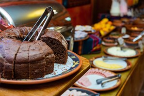 A buffet with a variety of food items including a chocolate cake with a knife on a plate. - Hotel Pakaritampu (Ollantaytambo)