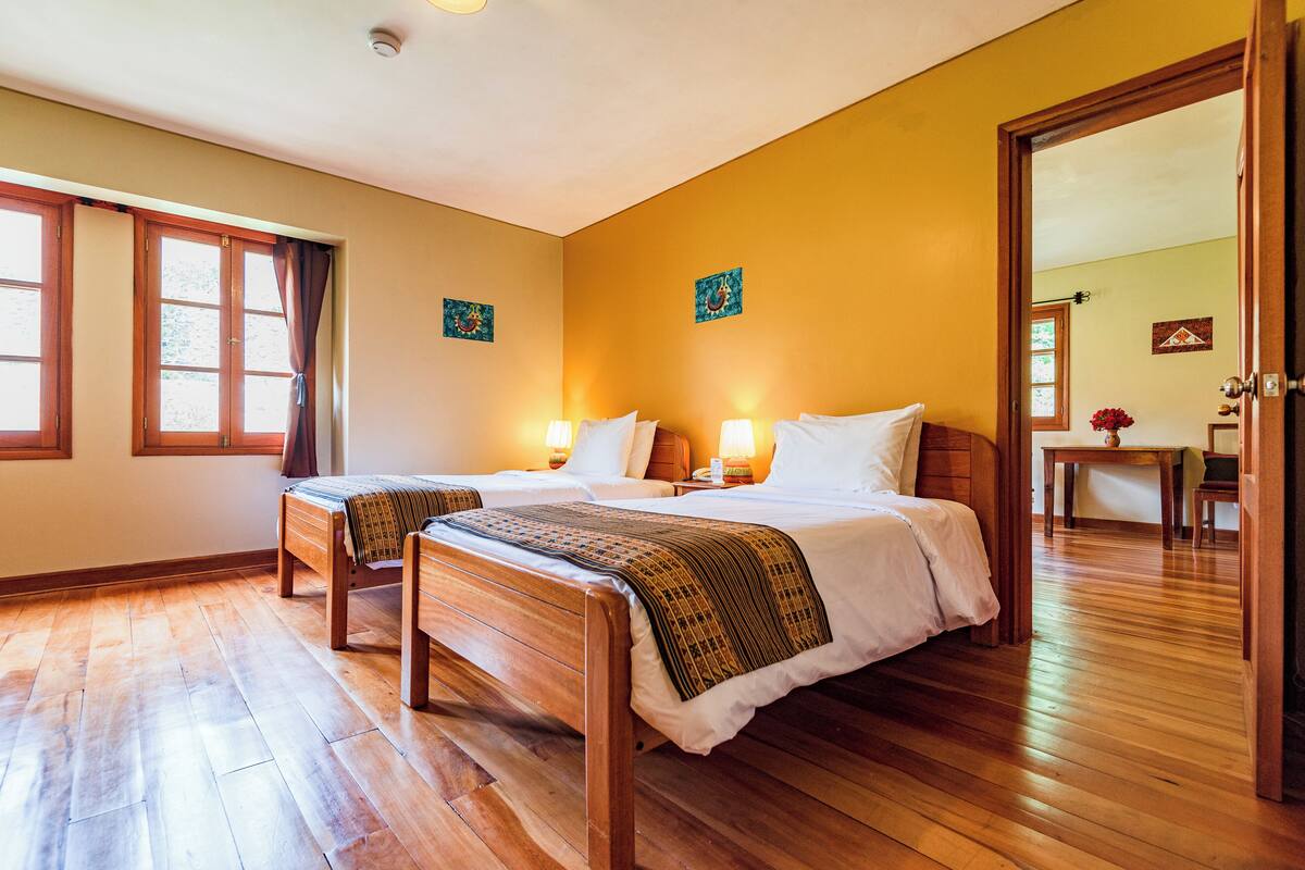 A hotel room with two wooden beds, a wooden floor, and a large window with curtains.