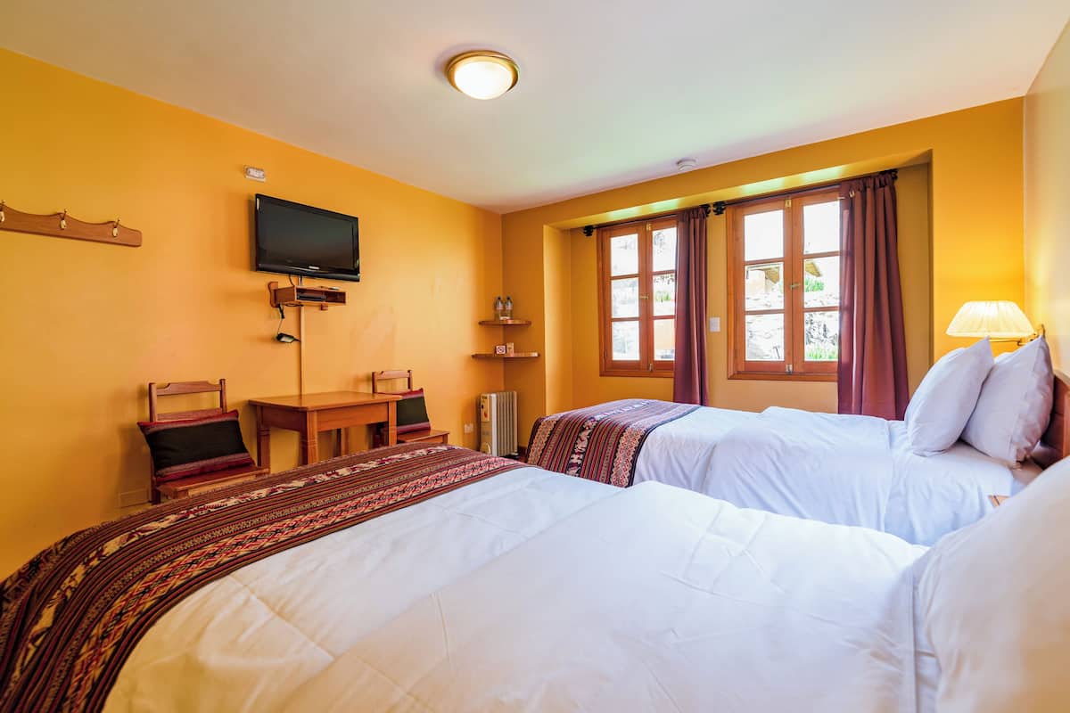 A hotel room with two beds, a television, a desk, and a window with curtains.