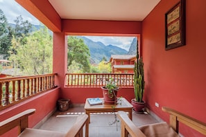 A balcony with a wooden table, chairs, a potted plant, and a view of mountains and a traditional building. - Hotel Pakaritampu (Ollantaytambo)