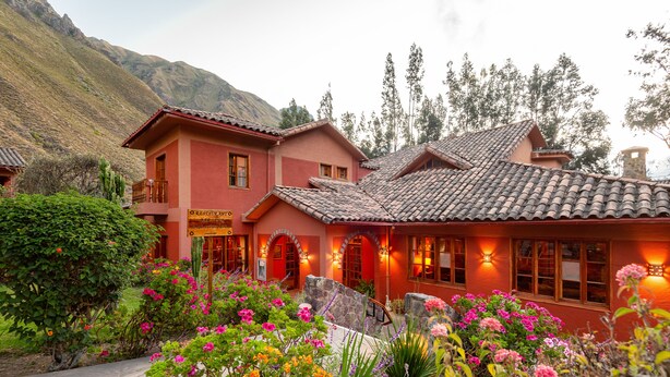 A two-story building with a red facade, a balcony, and a garden with colorful flowers. - Hotel Pakaritampu (Ollantaytambo)