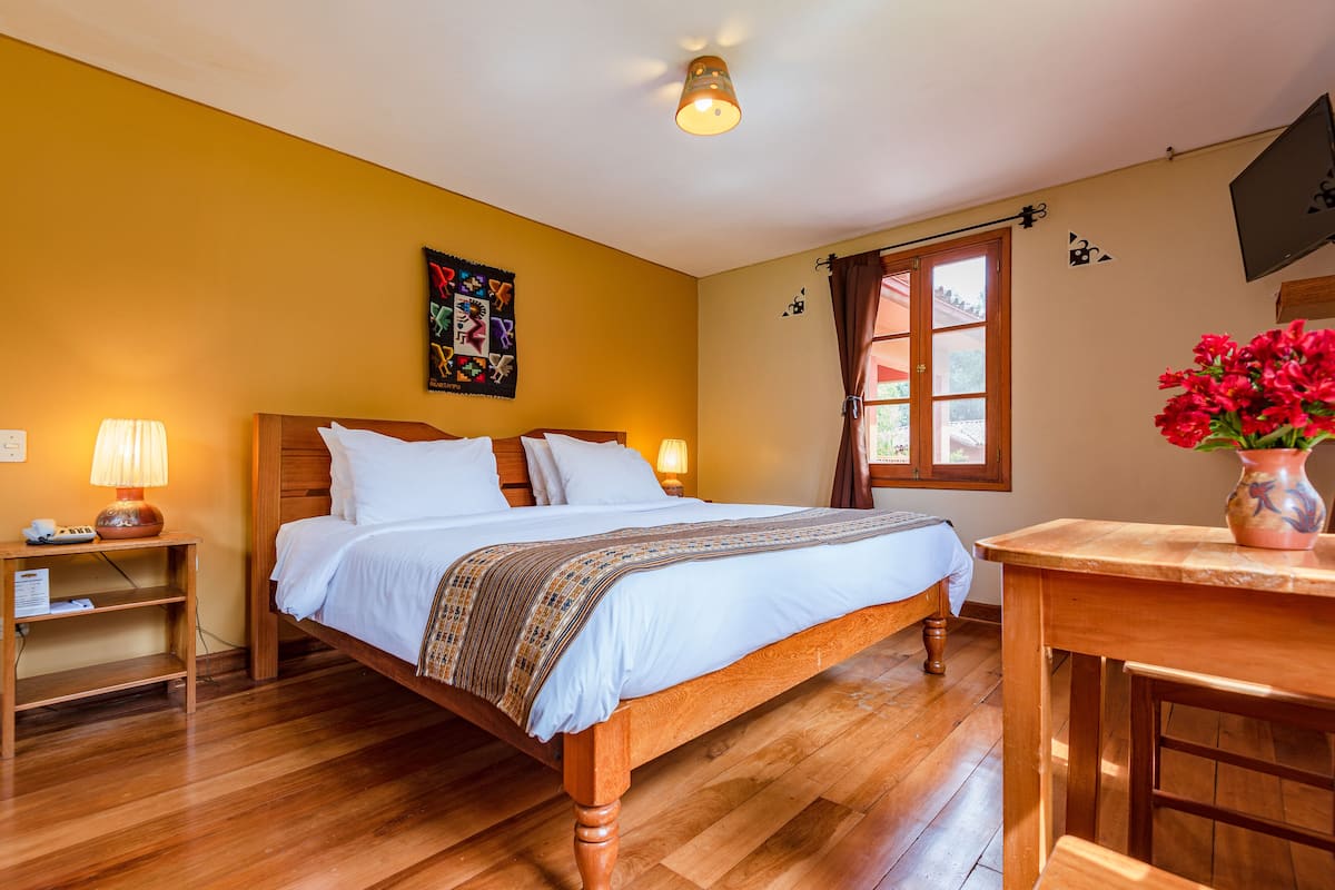 A neatly made bed with a wooden frame, a bedside table with a lamp, and a window with curtains.