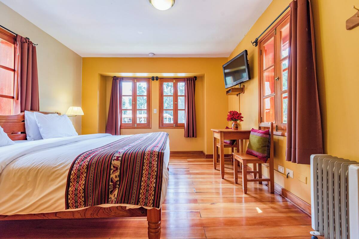 A hotel room with a bed, a desk, a chair, a TV, and large windows with curtains.