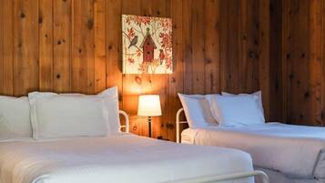 A room with two beds, a wooden wall, and a painting of birds and a house.