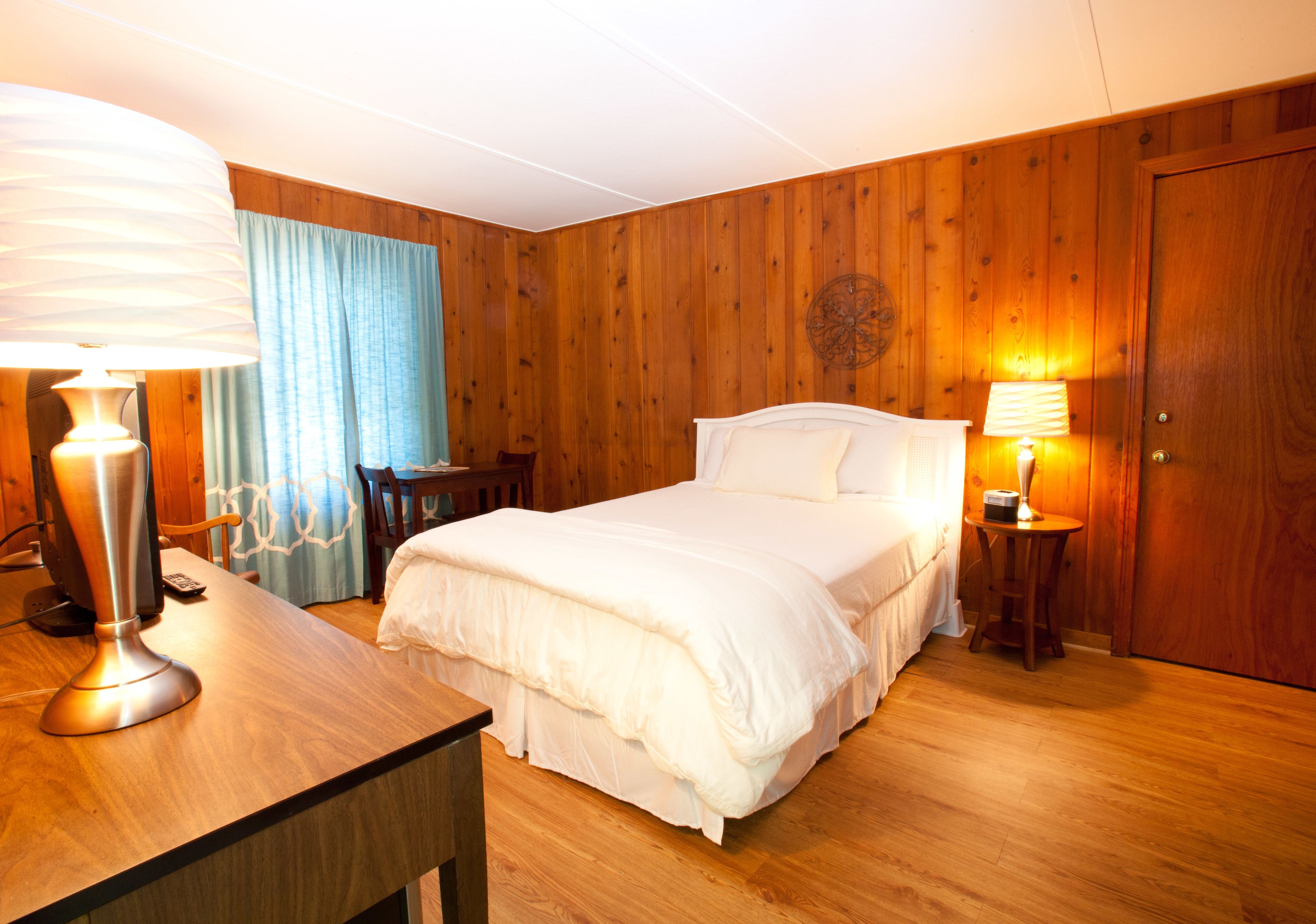 Ein Zimmer mit Holzwandverkleidung, einem Bett, zwei Nachttischlampen, einem Schreibtisch mit Lampe und einem Sessel.