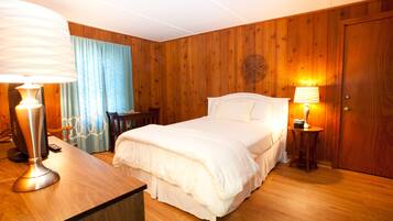 Ein Zimmer mit Holzwandverkleidung, einem Bett, zwei Nachttischlampen, einem Schreibtisch mit Lampe und einem Sessel.