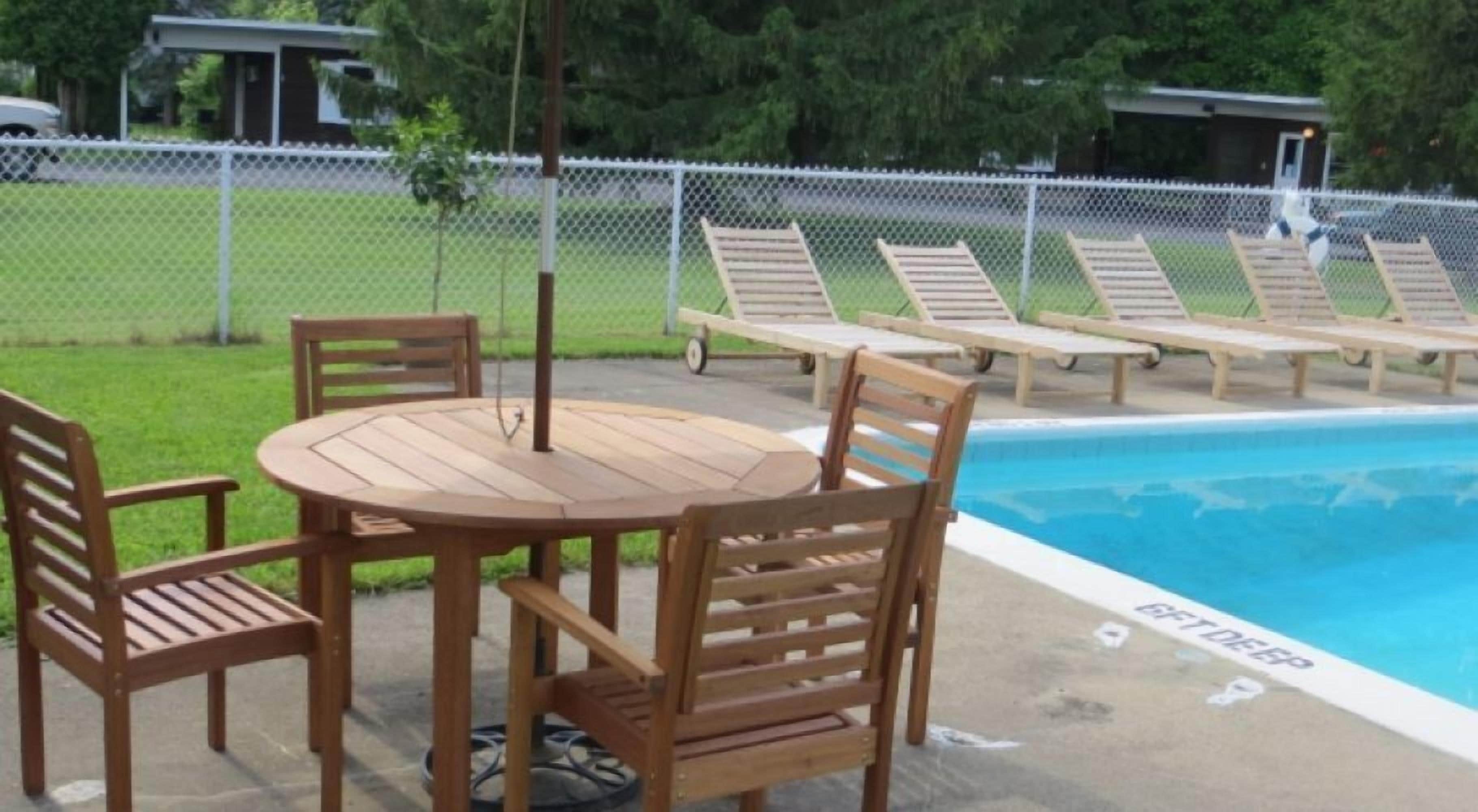 Een zwembadterras met een houten tafel en stoelen, ligbedden en een omheind zwembad.