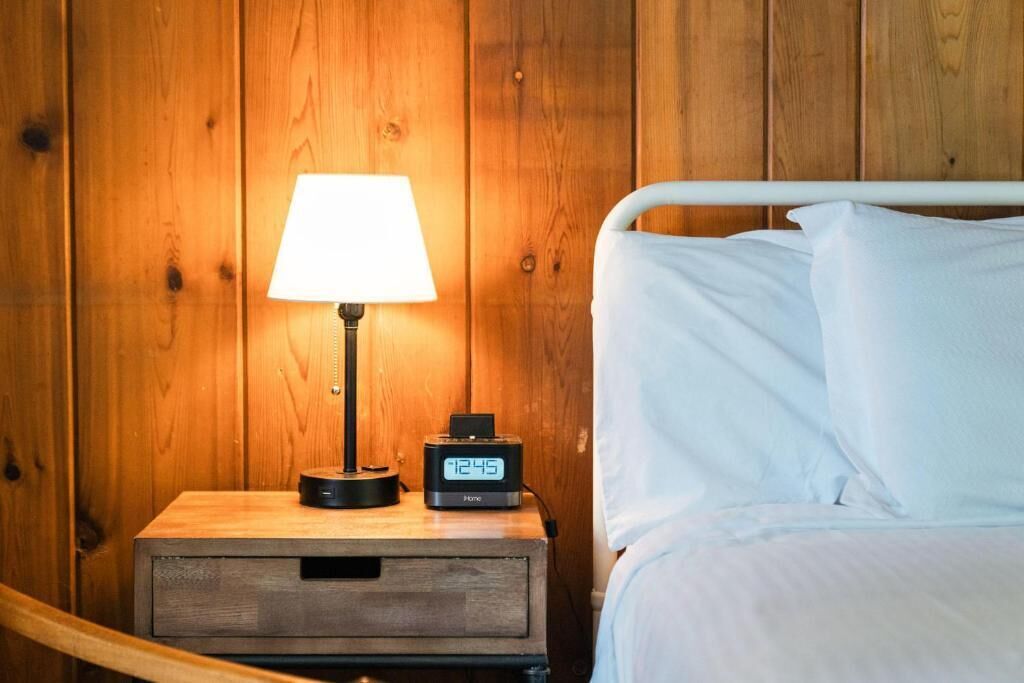 Ein Nachttisch aus Holz mit einer Lampe und einer digitalen Uhr, die 12:45 Uhr anzeigt.