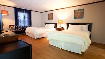 Habitación de hotel con dos camas, suelo de madera, un escritorio con computadora y una ventana con cortinas.