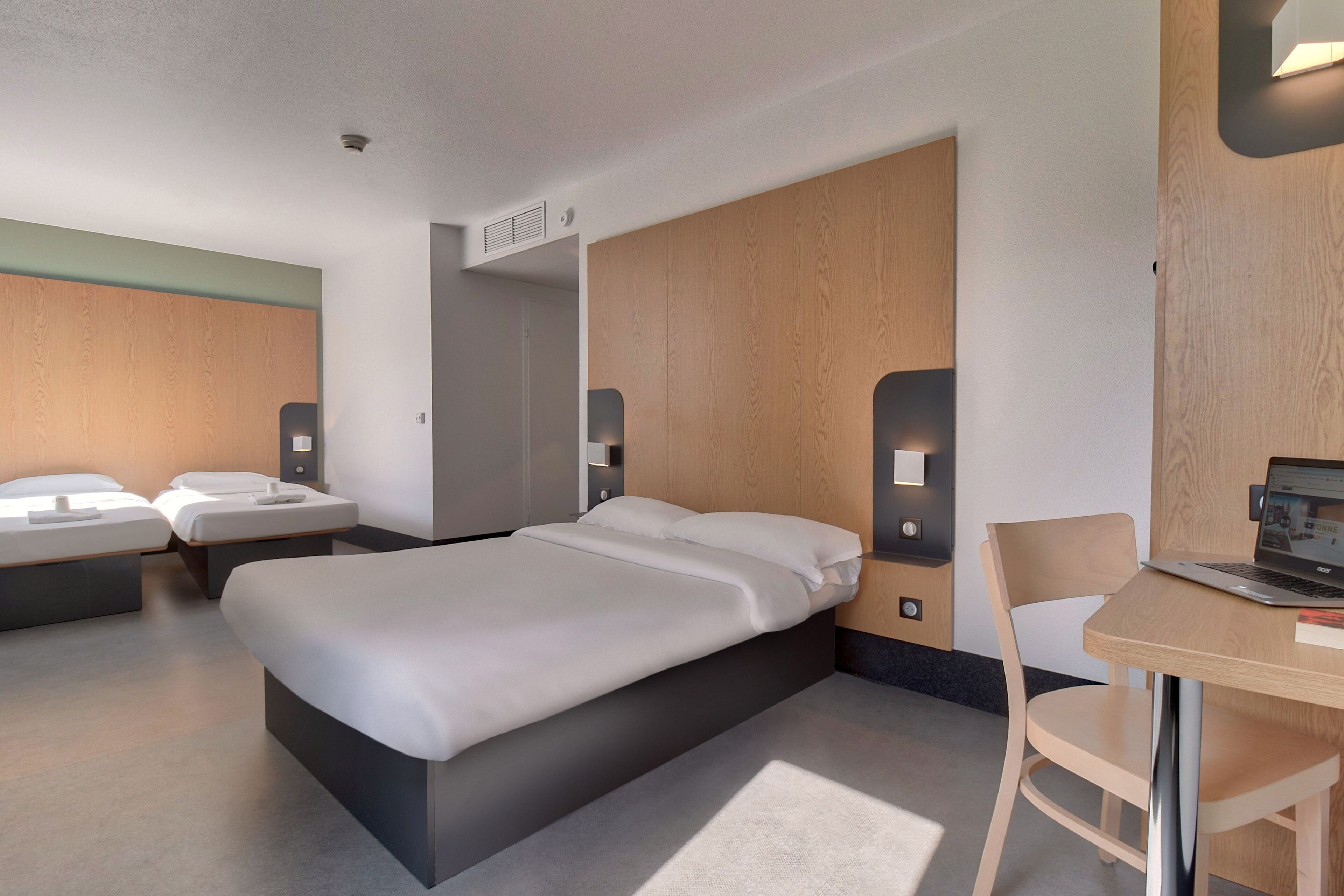 Et moderne hotelværelse med en stor seng, to sengeborde, et skrivebord med en bærbar computer og en stol.