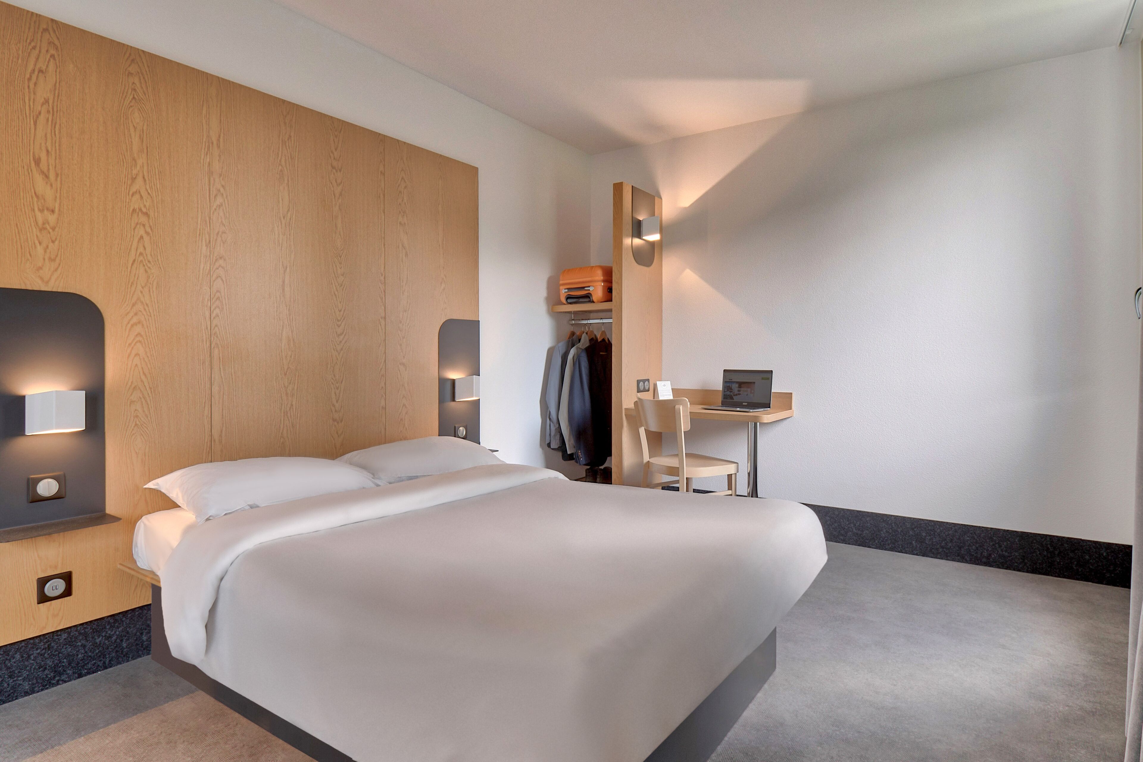 A modern hotel room with a large bed, a desk, and a wardrobe.