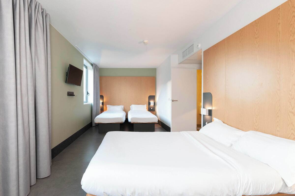 Una habitación de hotel con una cama grande, dos camas más pequeñas, un televisor y un panel de madera decorativo.