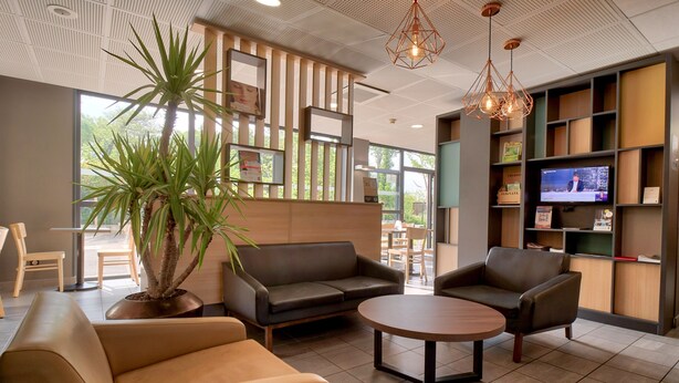 A modern lobby with leather sofas, a round table, a potted plant, and a television on a shelf.