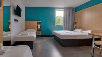 Habitación de hotel con dos camas, un escritorio, televisión y ventana con cortinas.