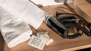 A neatly folded white towel, a black hairdryer, and a pamphlet on a wooden surface.