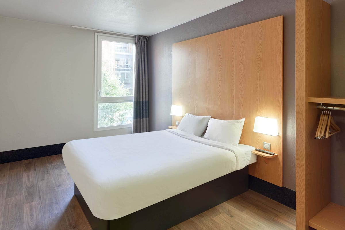 Ein modernes Hotelzimmer mit einem großen Bett, einem Holzkopfende, Nachttischlampen und einem Fenster mit Vorhängen.