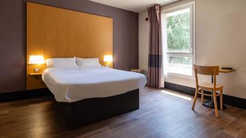 Habitación de hotel moderna con una cama grande, lámparas de noche, un cabecero de madera, una mesita y una silla.