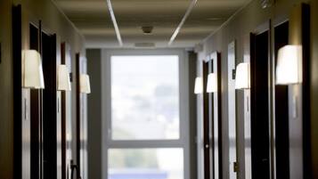 Un corridoio d'albergo con porte su entrambi i lati, ognuna illuminata da un punto luce.