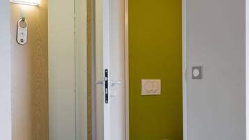 A hotel room with a wooden door, a mirror, a light fixture, a toilet, and a green wall.