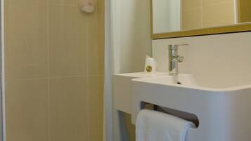 Un bagno con doccia, lavandino, specchio e portasciugamani.