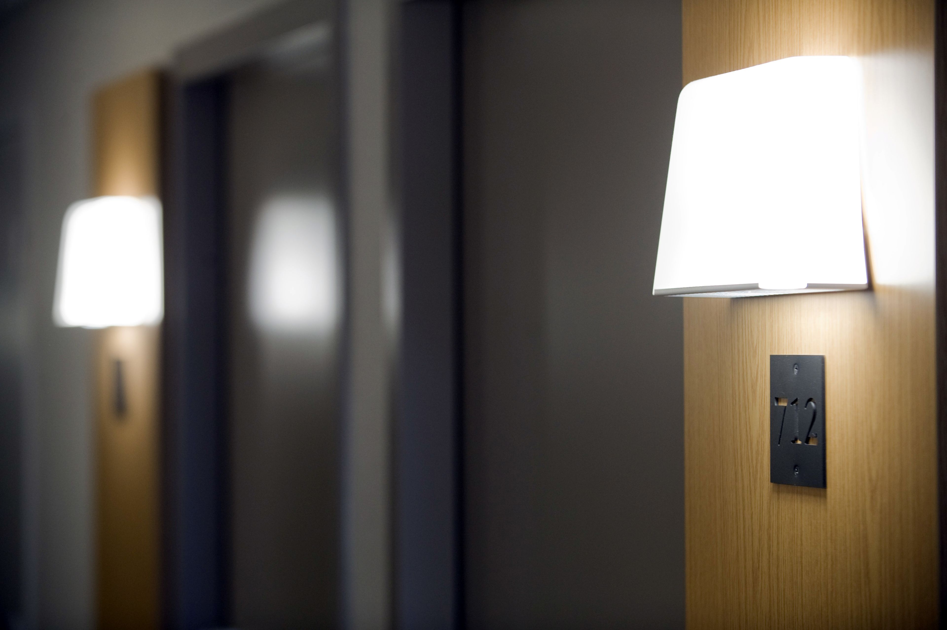 A hallway with wall-mounted lighting fixtures and a door with a switch.