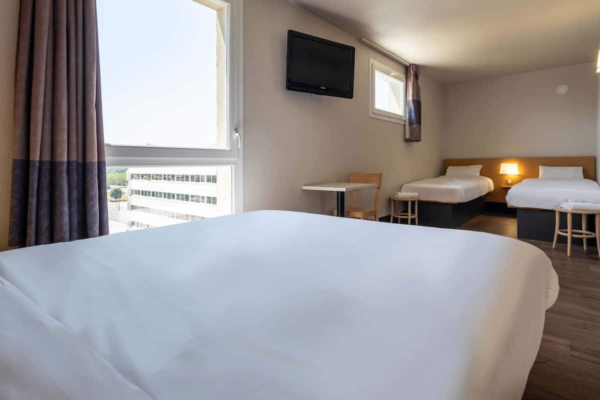 A hotel room with a large bed, two smaller beds, a TV, a table, and a chair.