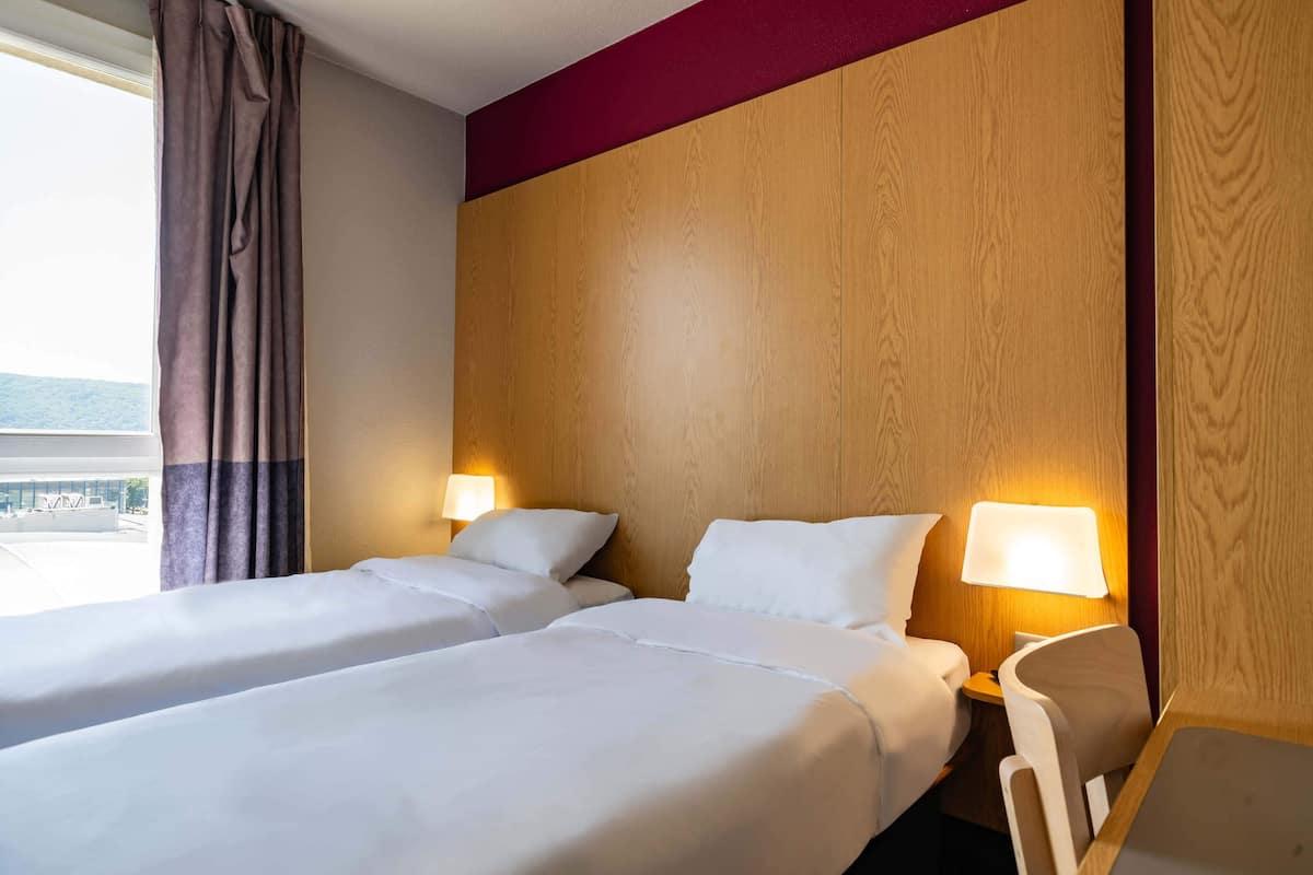 A hotel room with two beds, a wooden headboard, and two bedside lamps.