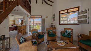 Un amplio salón con muebles de mimbre, una escalera y vistas al exterior.