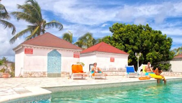 Una piscina con agua cristalina, sillas de descanso y pequeños edificios con tejados rojos.