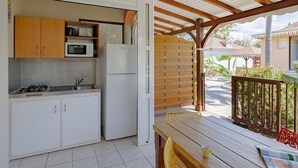 Una cocina compacta con armarios blancos, un microondas y un refrigerador. Hay una mesa de madera con una silla y una taza amarilla sobre ella.