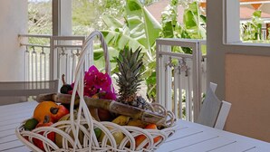 Un porche cubierto con una mesa que presenta una cesta de mimbre llena de frutas y flores.