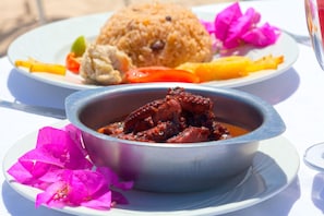 A meal consisting of rice, vegetables, and a bowl of stew, served on a white table with a glass of water and pink flowers.