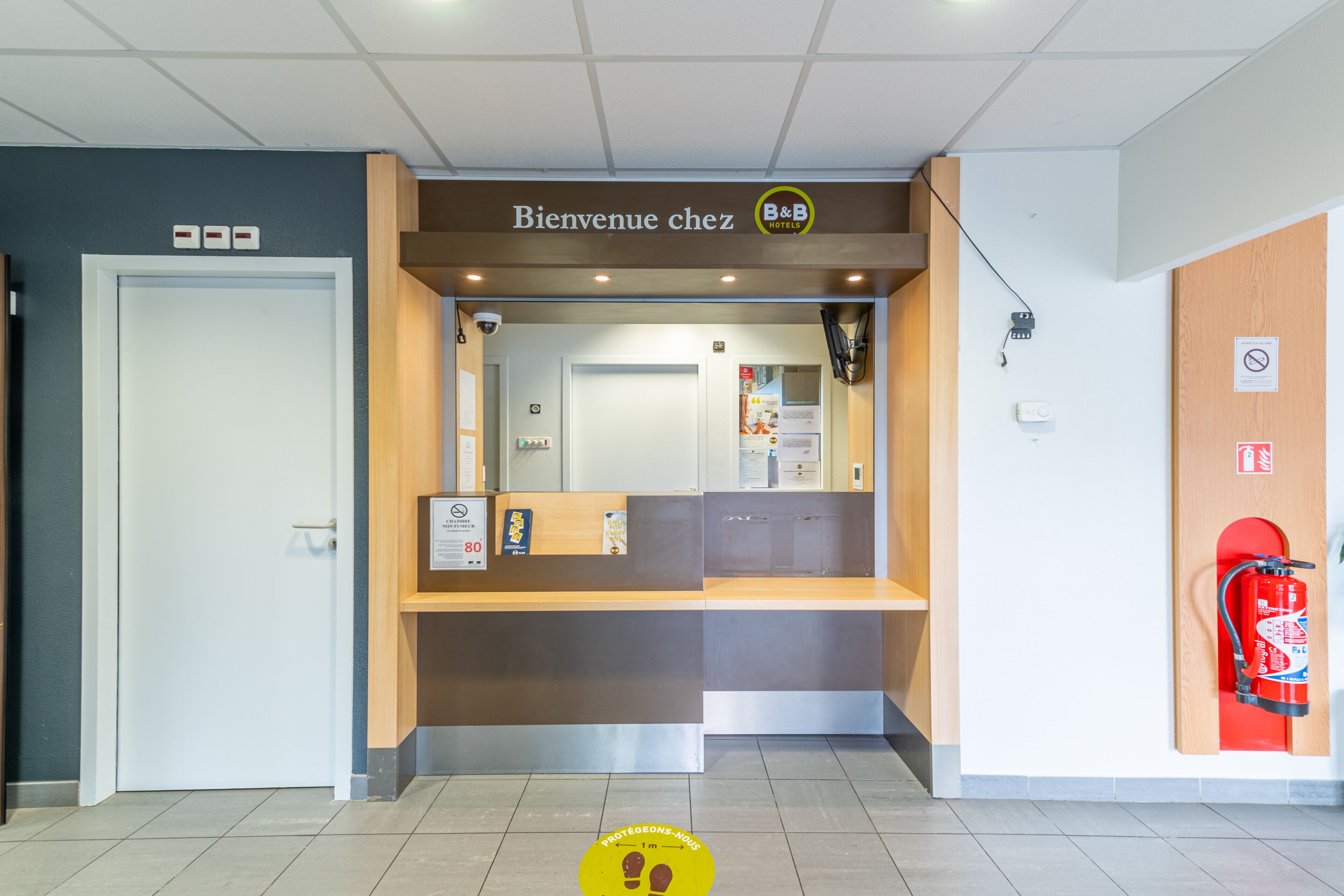 A reception desk with a sign reading "Bienvenue chez B&B HOTELS" and a fire extinguisher mounted on the wall.