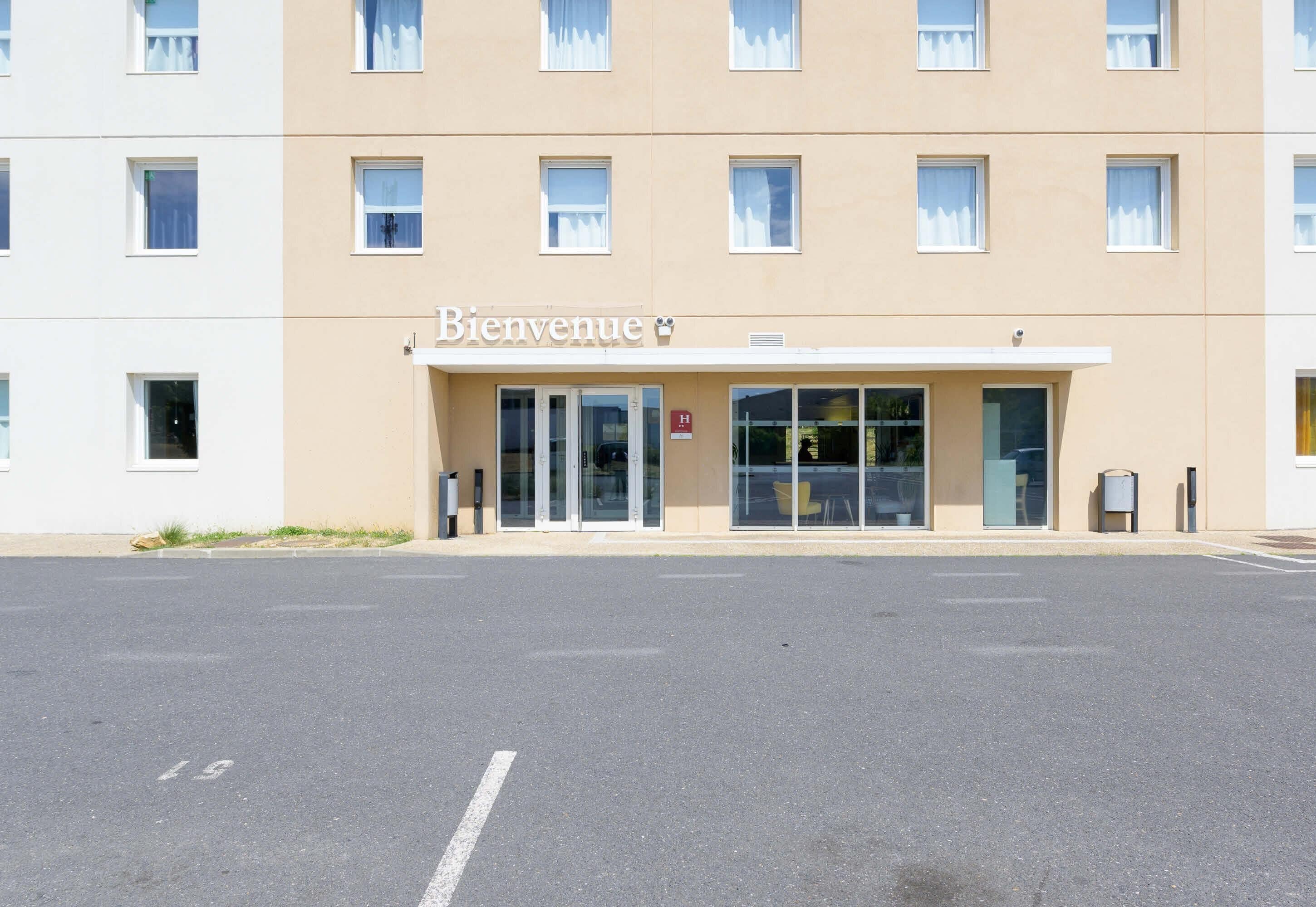 A building with a 'Bienvenue' sign, large windows, and a parking lot.