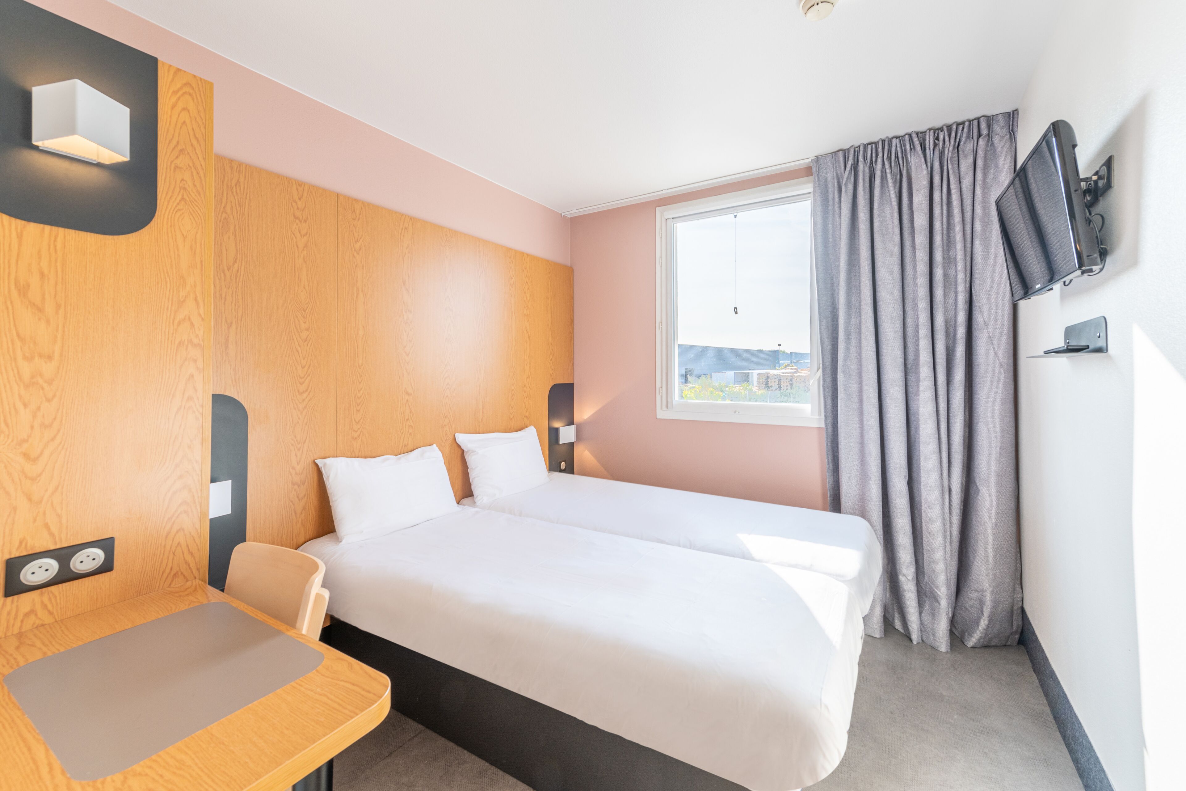 Habitación de hotel con dos camas, un escritorio, un televisor y una ventana con cortinas.