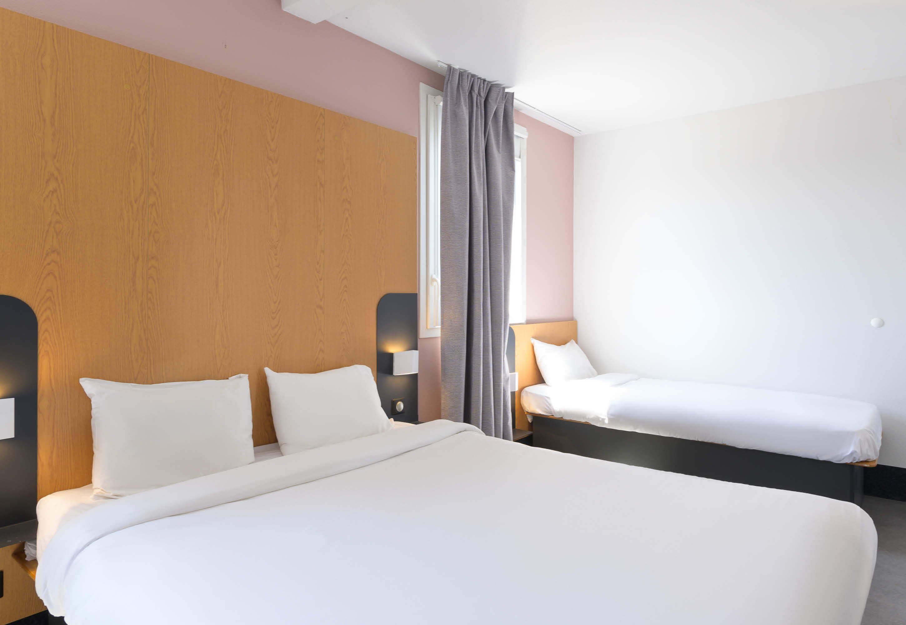 A hotel room with a large bed, a smaller bed, and a nightstand with a lamp.