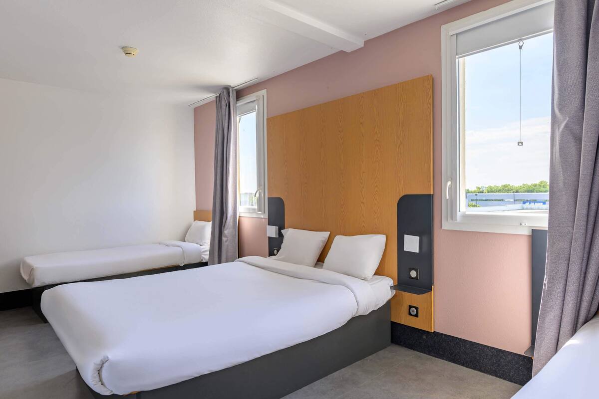 A hotel room with two beds, a wooden headboard, a window with curtains, and a view of a body of water.