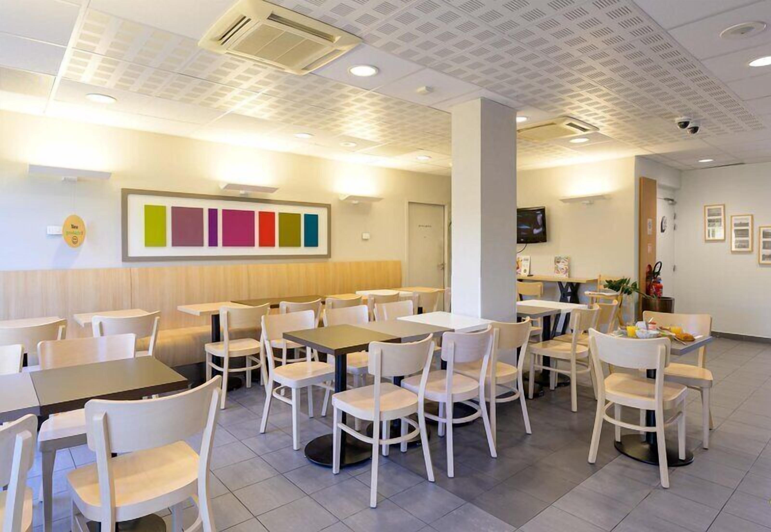 A dining area with tables and chairs, a wall-mounted TV, and a ceiling with recessed lighting.