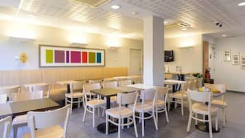 A dining area with tables and chairs, a wall-mounted TV, and a ceiling with recessed lighting.