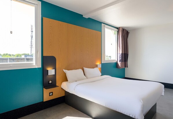 A hotel room with a bed, two bedside lamps, a window, and a wall-mounted light. - B&B HOTEL Lieusaint Carré Sénart (Lieusaint)