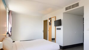 Een moderne hotelkamer met een bed, een aan de muur bevestigde televisie en een deur naar een andere kamer.