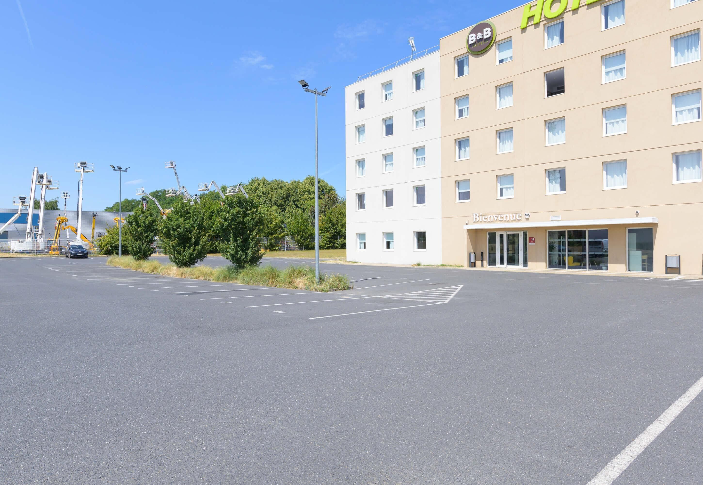 A hotel with a 'B&B' sign, a 'Bienvenue' sign, and a parking lot.
