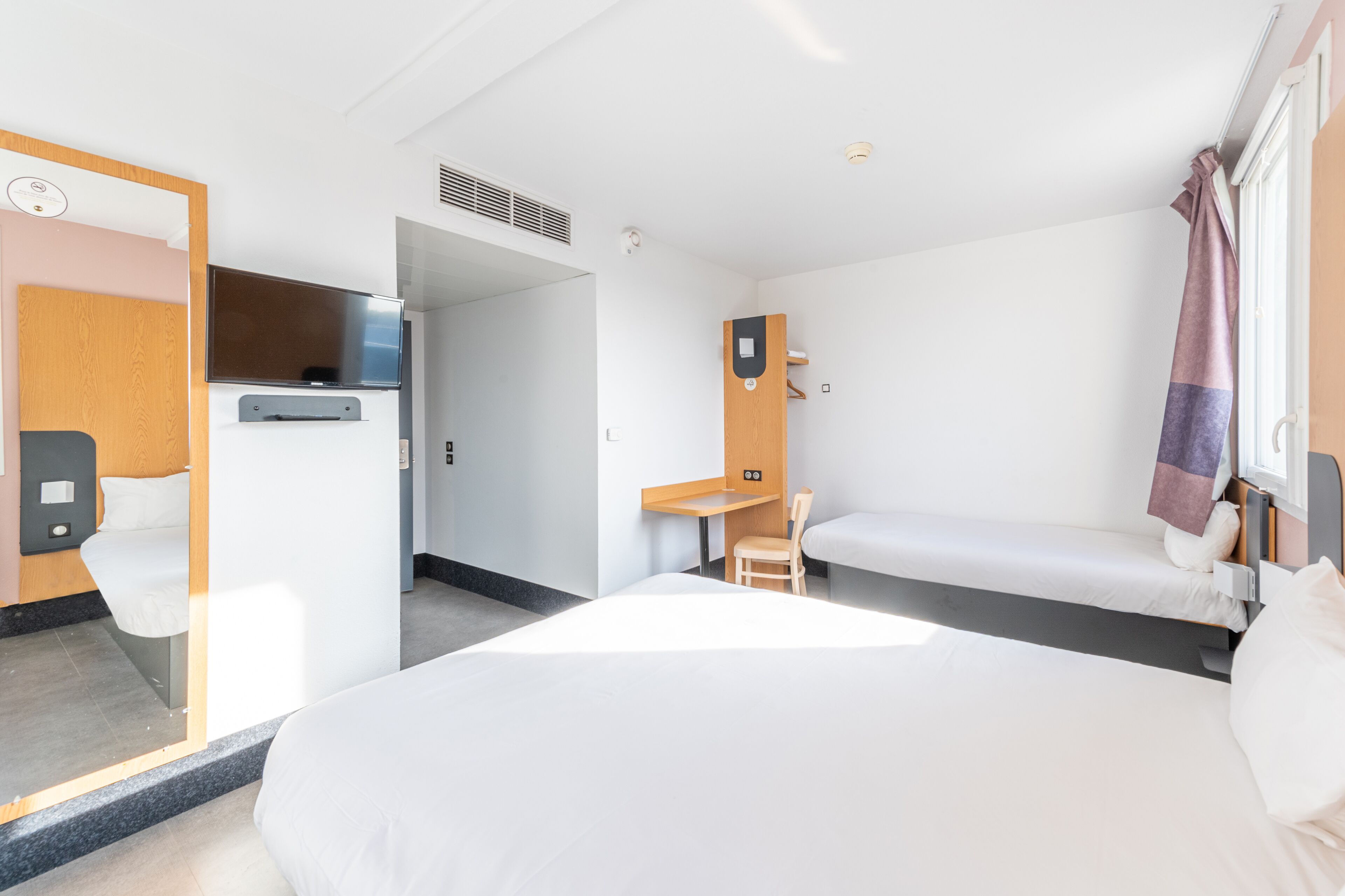 A hotel room with a large bed, a desk, a chair, a TV, and a bathroom door.