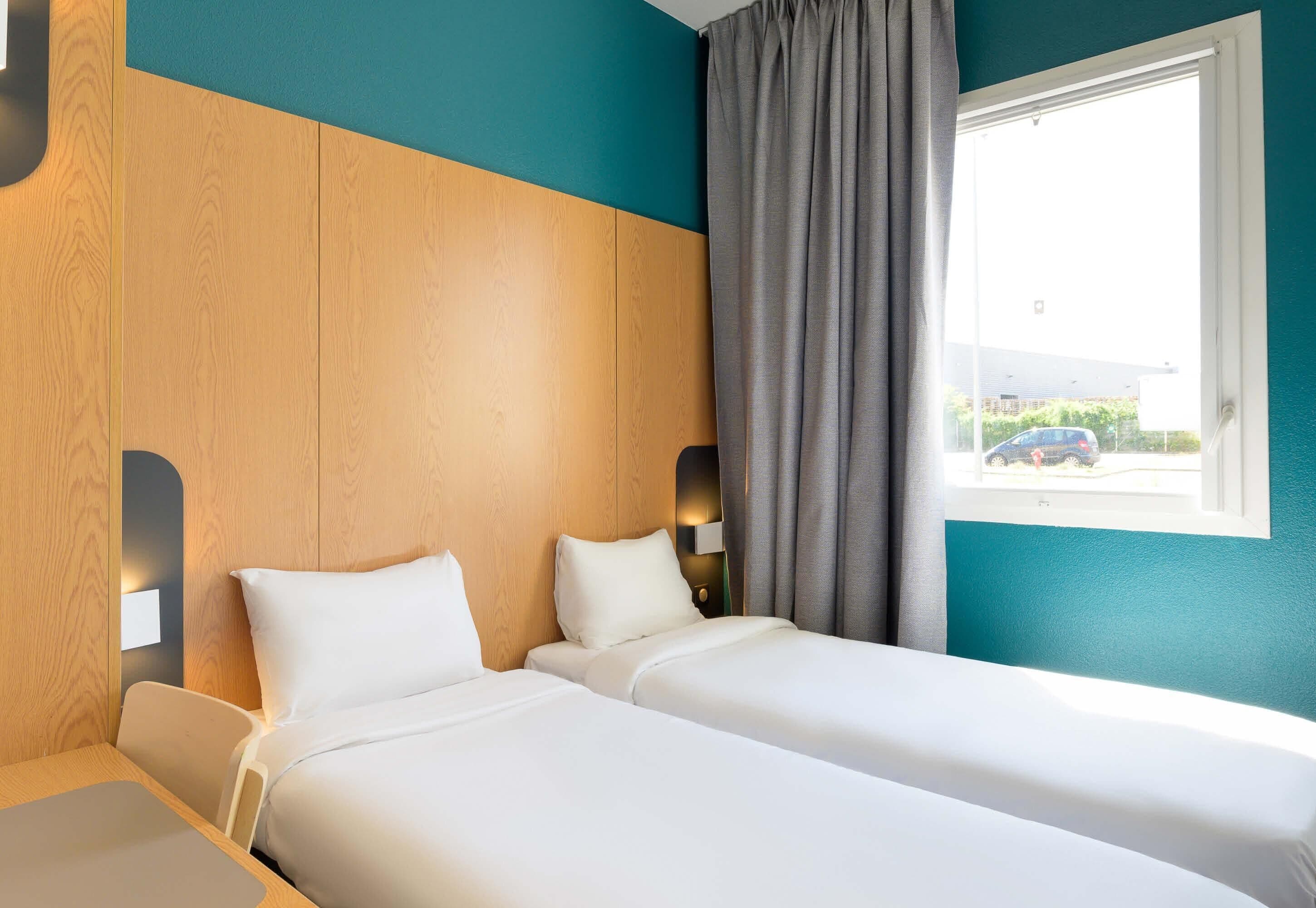 Habitación de hotel con dos camas, una ventana con cortinas y vistas al exterior.