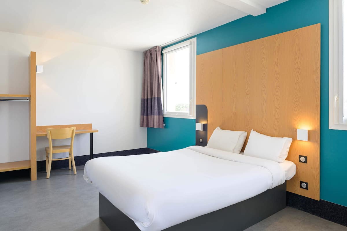 A hotel room with a bed, a desk, and a chair.