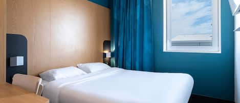Habitación de hotel con cama, escritorio, ventana con cortinas y vista al cielo.