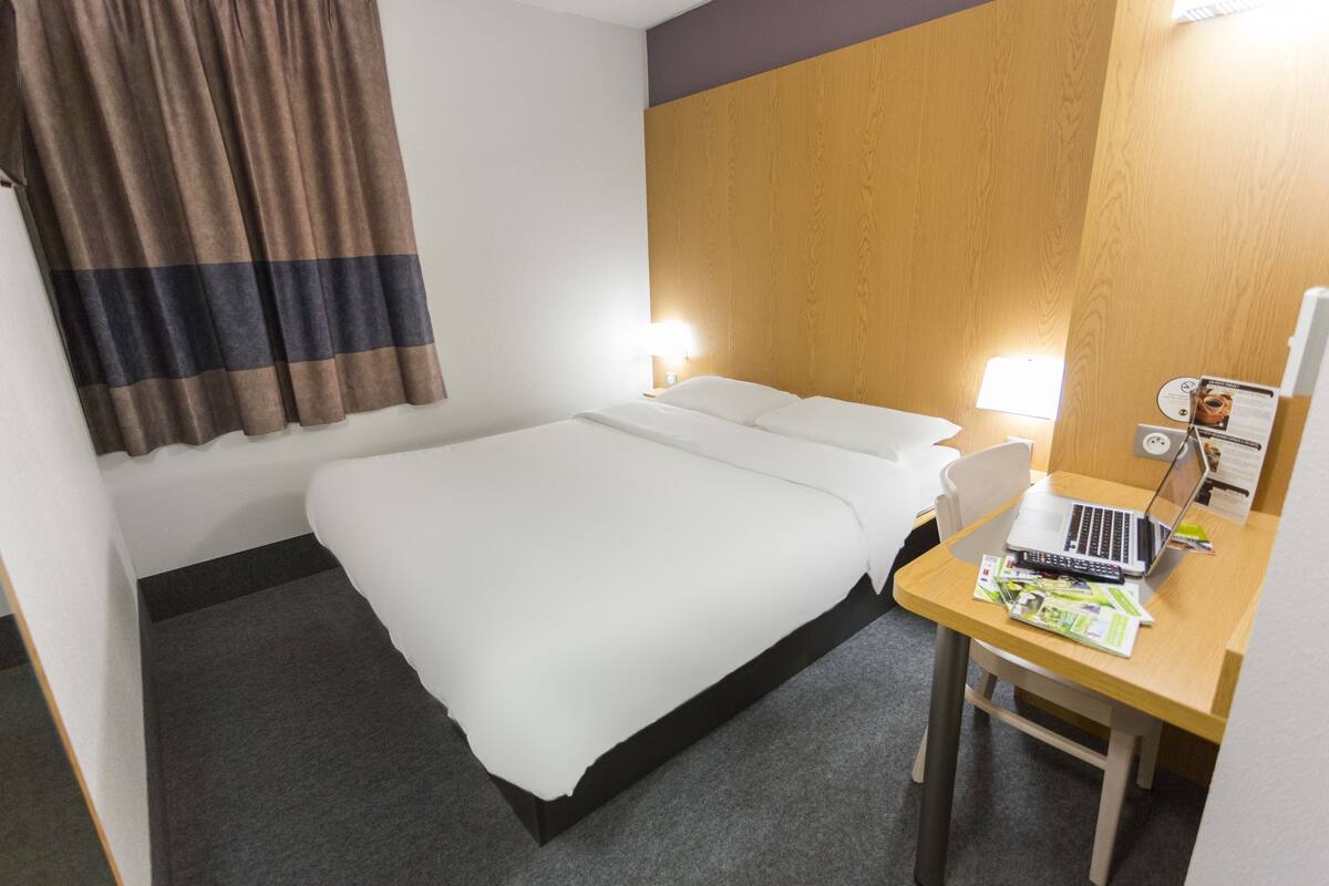 A hotel room with a bed, a desk with a laptop, and a chair.