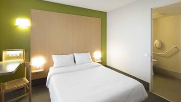 Une chambre d’hôtel avec un lit, une table de chevet, une chaise et une salle de bain visible à travers une porte ouverte.