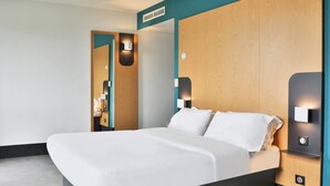 A modern hotel room with a large bed, wooden headboard, and built-in wall sconces.